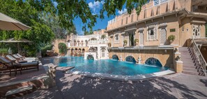 A pool area with lounge chairs, a fountain, and a building with ornate architecture. -  Ajit Bhawan - A Palace Resort (Jodhpur)