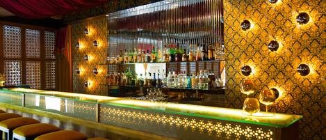 A bar with a patterned wall, a red curtain, and a bar counter with stools.
