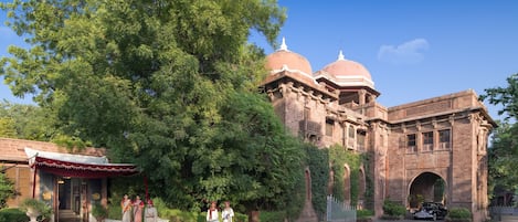 A historic building with domed architecture, a paved entrance, and a tree-lined driveway.