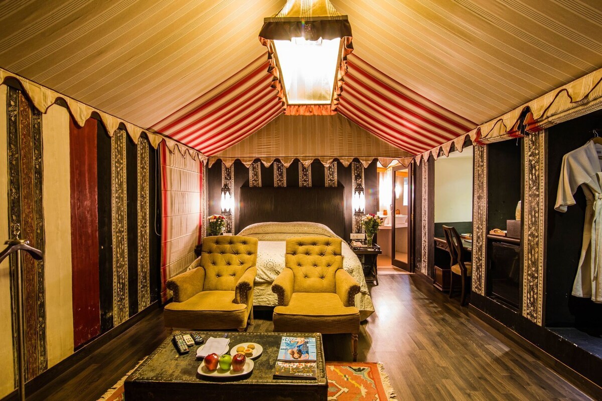 A room with a large bed, two armchairs, a small table with snacks, a mirror, and a robe hanging on the wall.