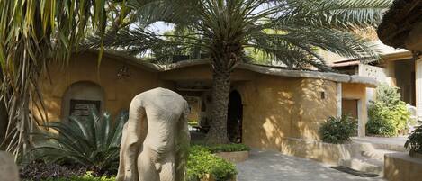 A courtyard with a palm tree, a large stone sculpture, and a building with arches.