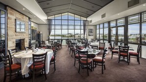 Un restaurante con varias mesas y sillas, una pared de piedra y amplios ventanales con vistas.