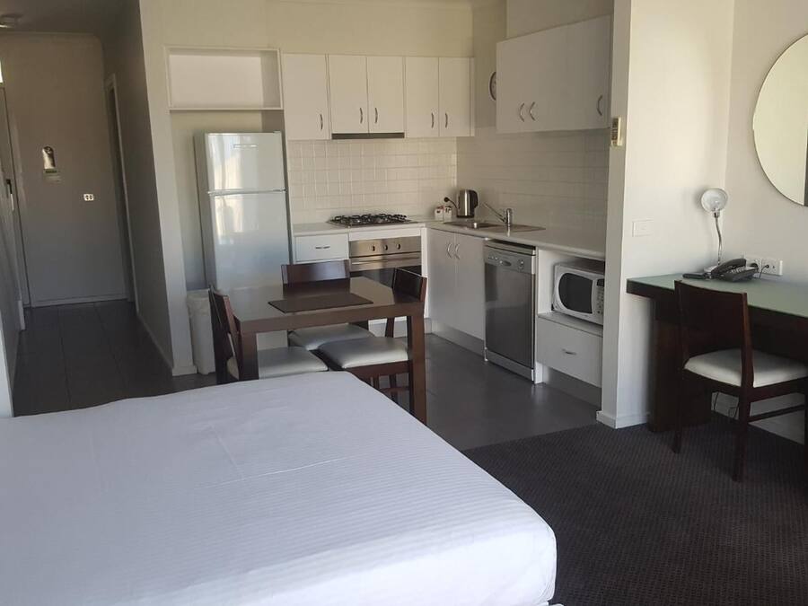 A hotel room with a bed, a desk, a chair, a microwave, a stove, and a sink.