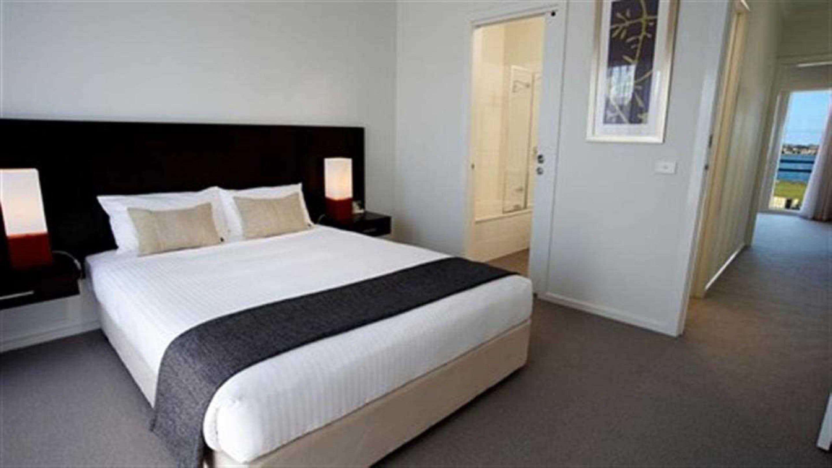 A hotel room with a large bed, two bedside tables, a nightstand, a door, and a framed picture on the wall.