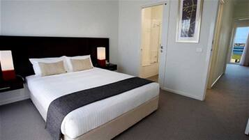 A hotel room with a large bed, two bedside tables, a nightstand, a door, and a framed picture on the wall.