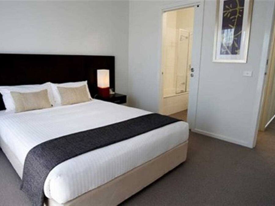 A hotel room with a large bed, two bedside tables, a nightstand, a door, and a framed picture on the wall.