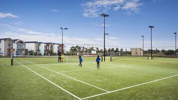 Una cancha de tenis exterior con red, rodeada de edificios y árboles.