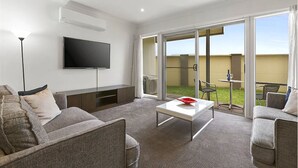 Habitación de hotel moderna con televisor de pantalla plana, sofá, mesa de centro y balcón con mesa y sillas.