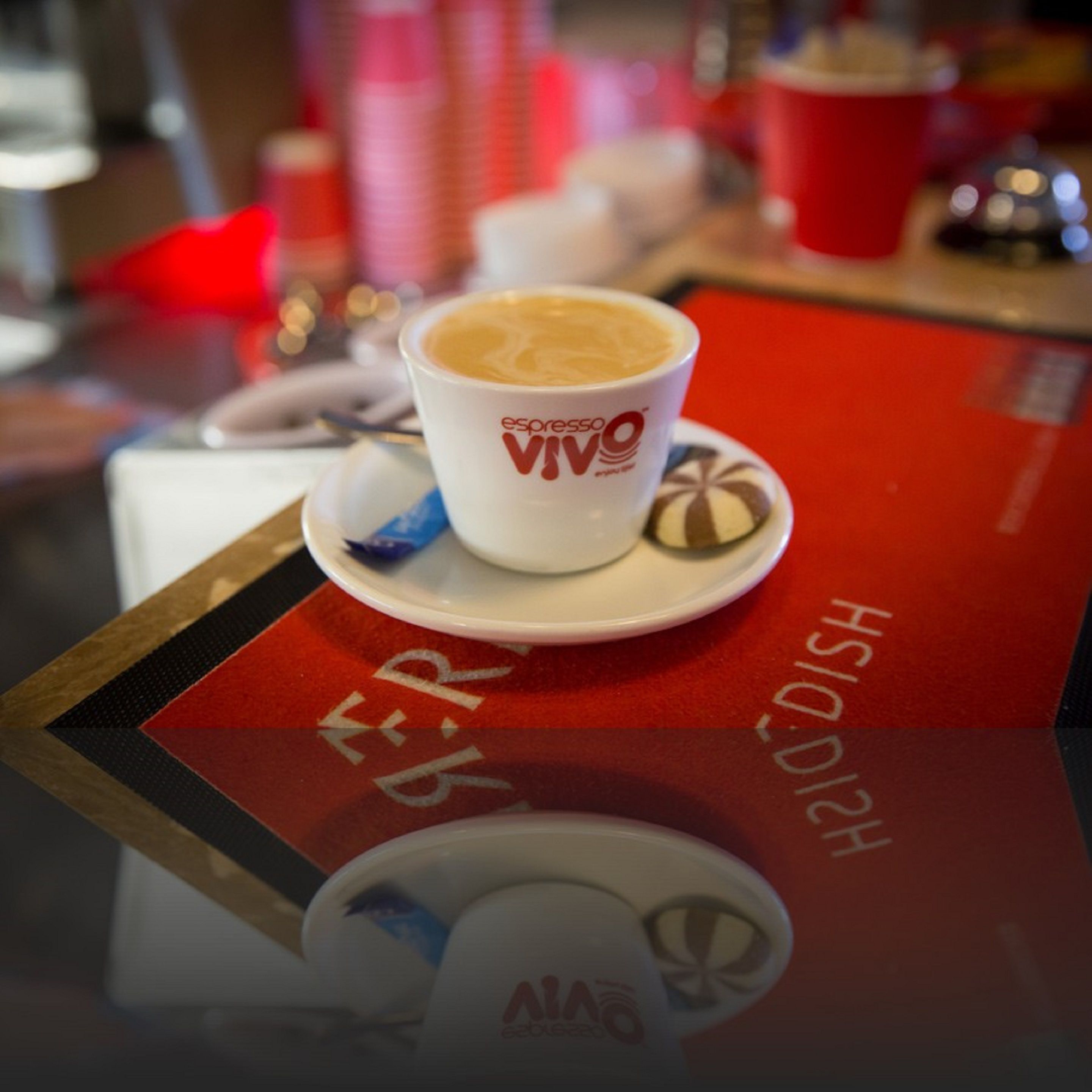 A cup of espresso on a saucer with a red tablecloth and a logo.