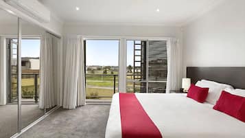 A hotel room with a large bed, a view of a golf course, and a balcony with a sliding door.