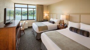 Une chambre d’hôtel avec deux lits, un bureau avec une télévision, une chaise et une vue sur un lac et des montagnes.