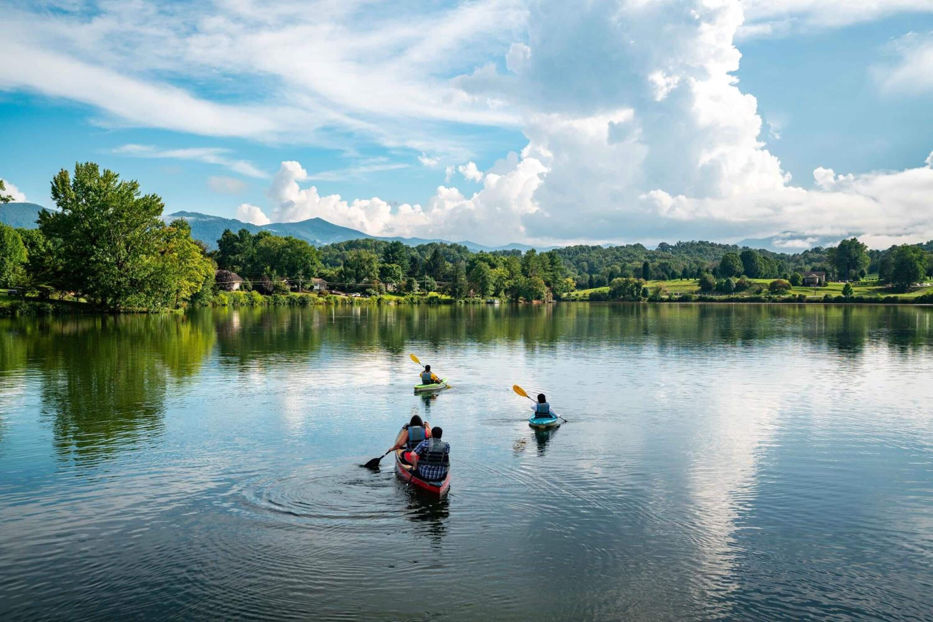 A calm lake with kayaks and a person paddling.