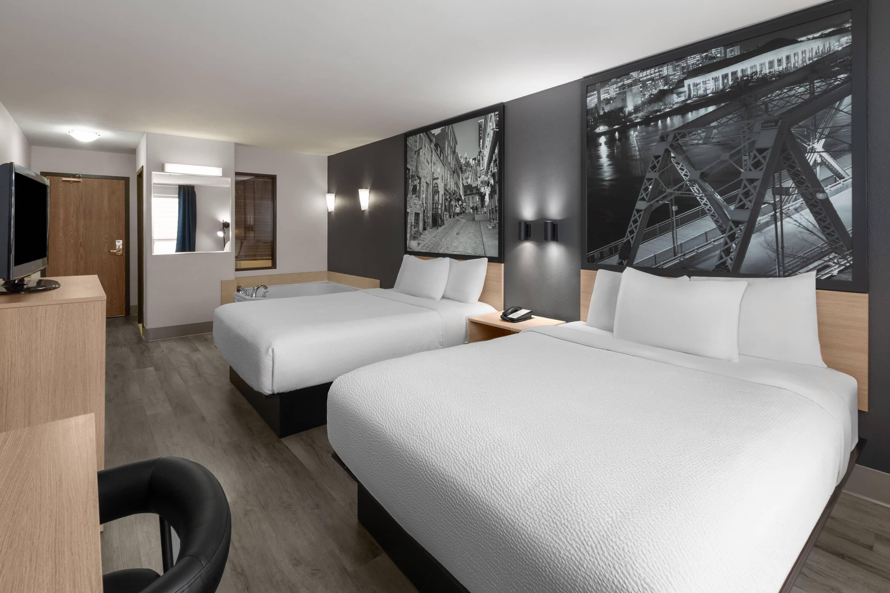 A hotel room with two beds, a desk with a TV, a mirror, and artwork on the walls.