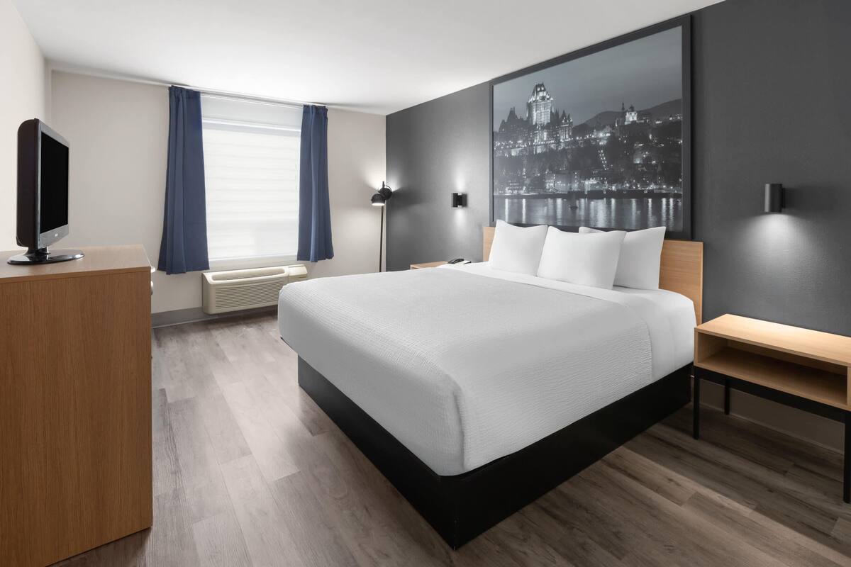 A modern hotel room with a large bed, a desk, a flat-screen TV, and a cityscape view.