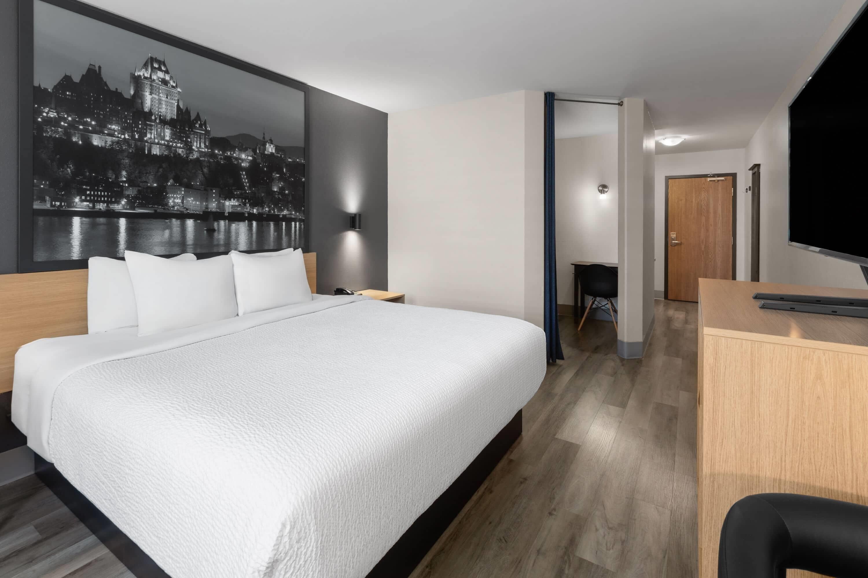 Una habitación de hotel moderna con una cama grande, un escritorio y un cuadro de paisaje urbano en la pared.