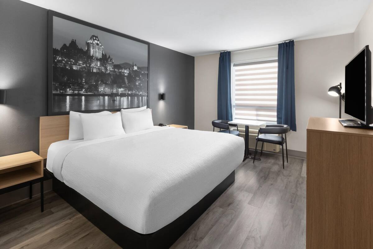 A modern hotel room with a large bed, a desk, a chair, a television, and a window with curtains.