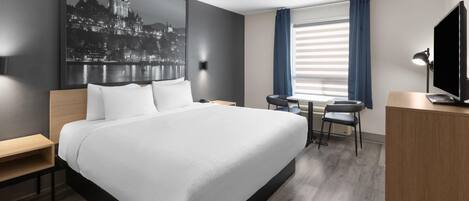 A modern hotel room with a large bed, a desk, a chair, a television, and a window with curtains.