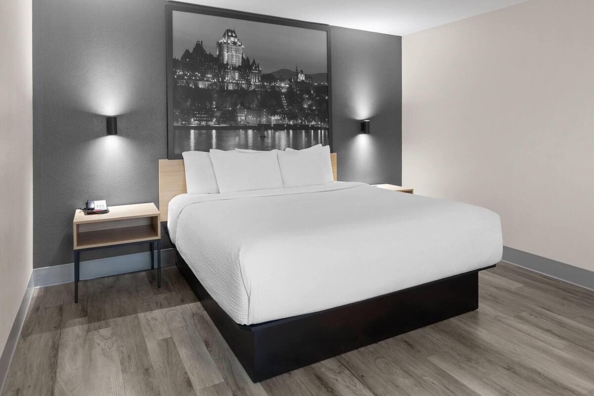 A modern hotel room with a large bed, two bedside tables, and a cityscape view.
