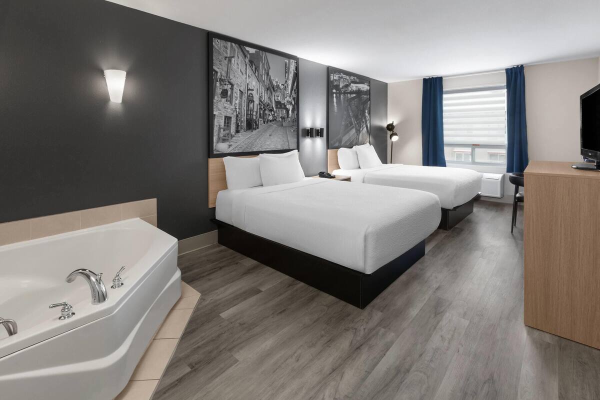A hotel room with two beds, a large bathtub, and a desk with a television.