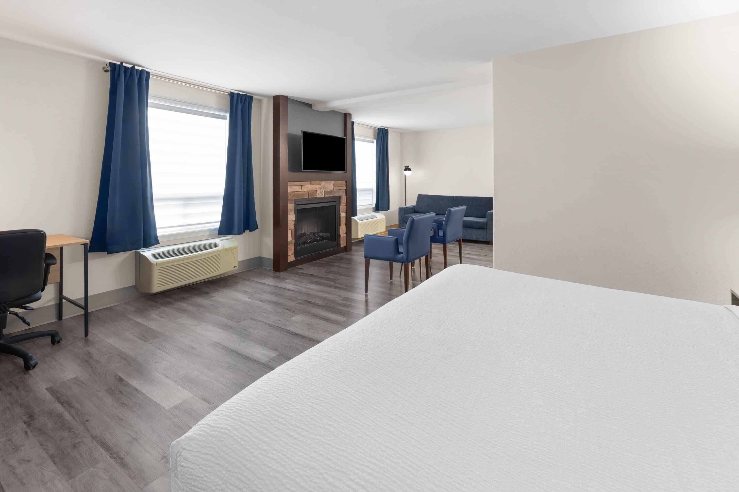 A hotel room with a bed, a desk, a chair, a sofa, a fireplace, and a TV.