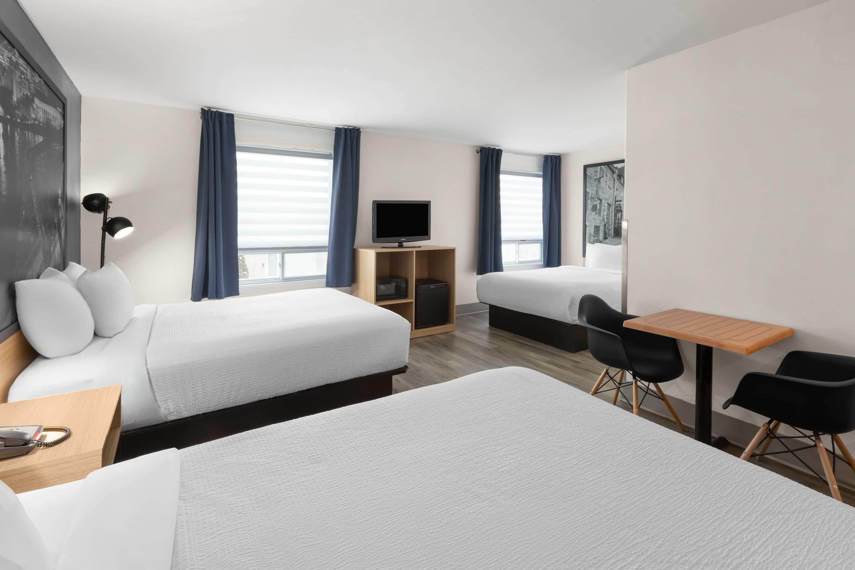 Habitación de hotel con dos camas, un escritorio, una silla, un televisor y una ventana con cortinas.