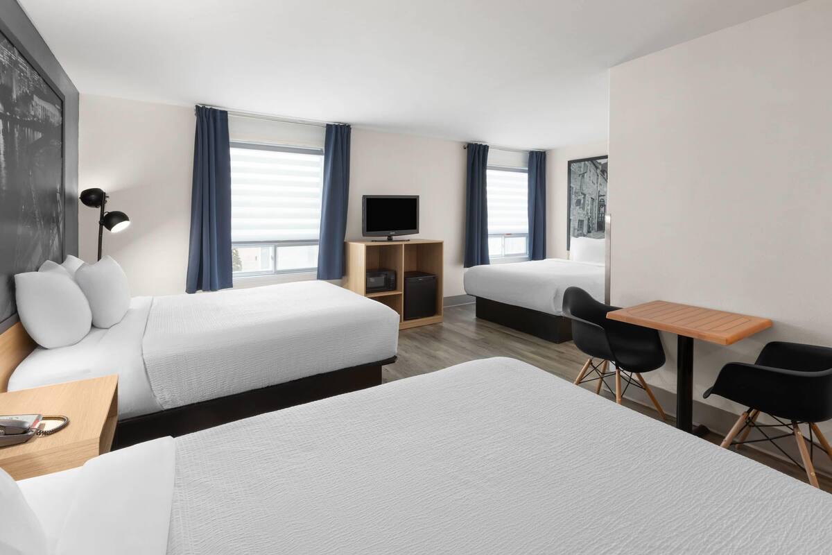 A hotel room with two beds, a desk, a chair, a TV, and a window with curtains.