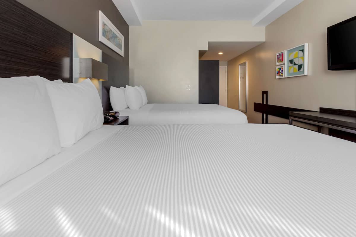 A hotel room with two beds, a flat-screen TV, artwork on the walls, and a door leading to another room.