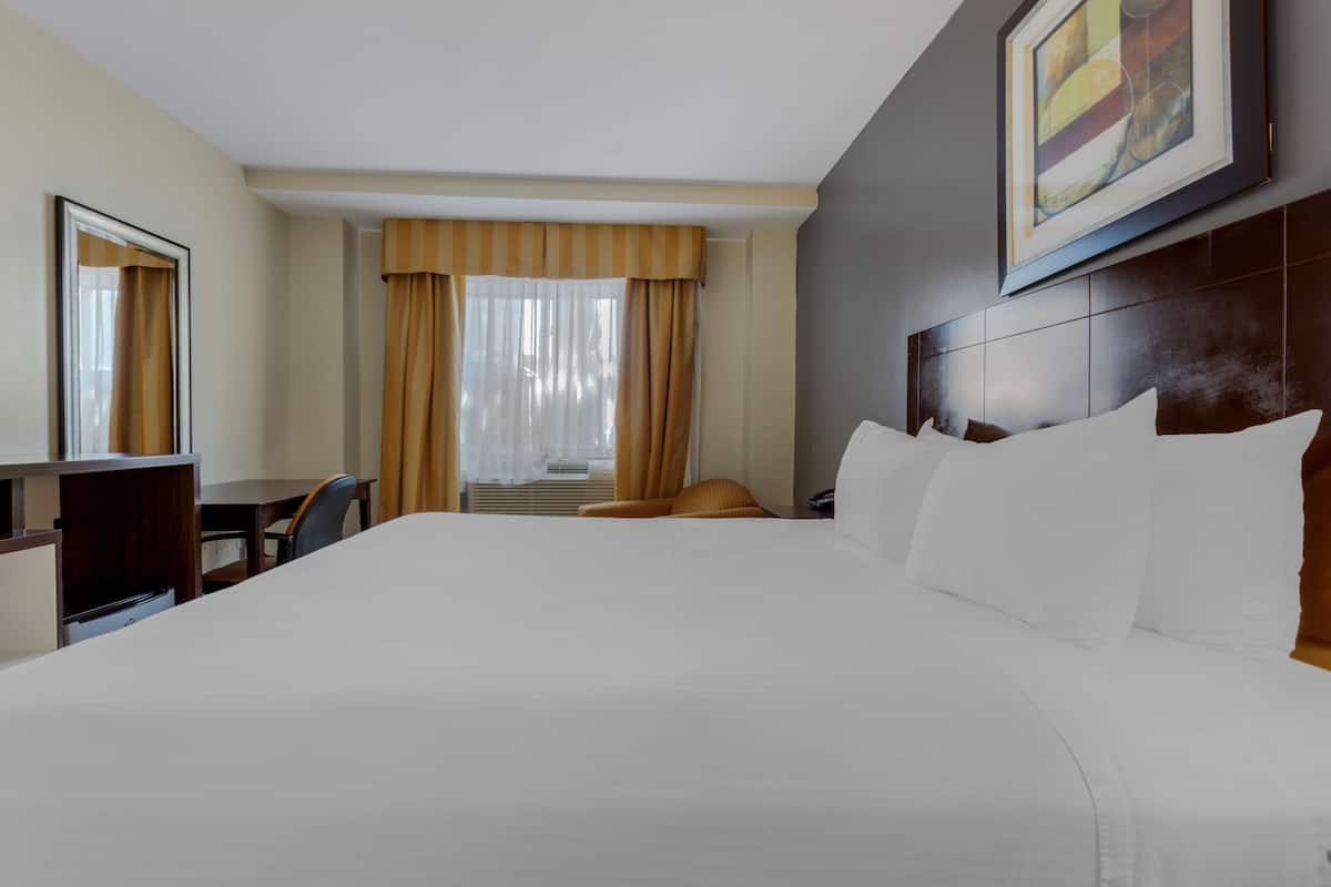 A hotel room with a large bed, a desk, a chair, and a window with curtains.