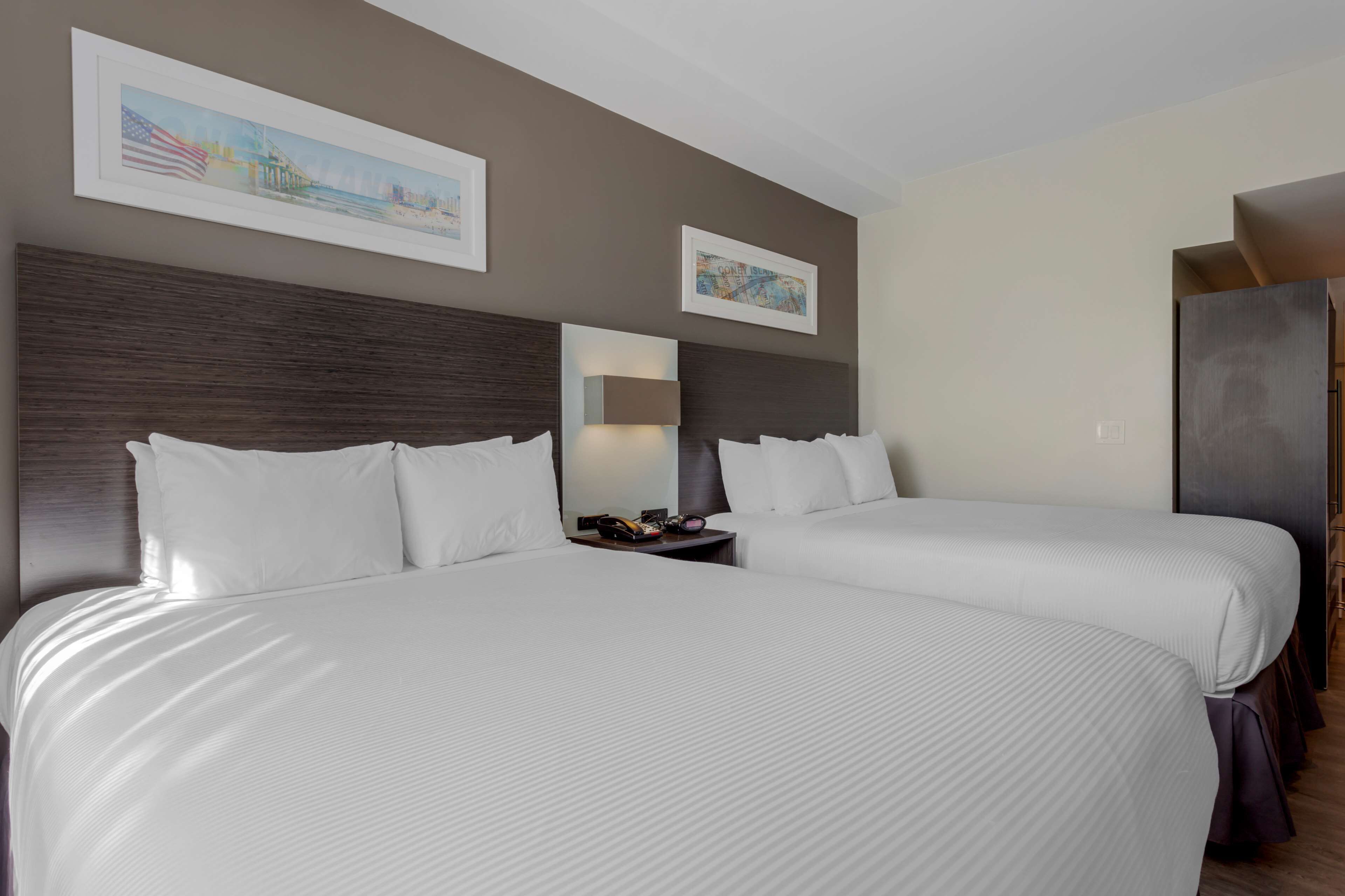 A hotel room with two beds, a nightstand, a mirror, and framed artwork on the walls.