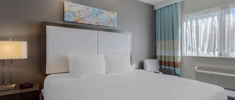 Una habitación de hotel con una cama grande, una mesita de noche con lámpara, un cuadro de un mapa en la pared y una ventana con cortinas.