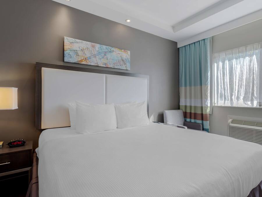 Una habitación de hotel con una cama grande, una mesita de noche con lámpara, un cuadro de un mapa en la pared y una ventana con cortinas.