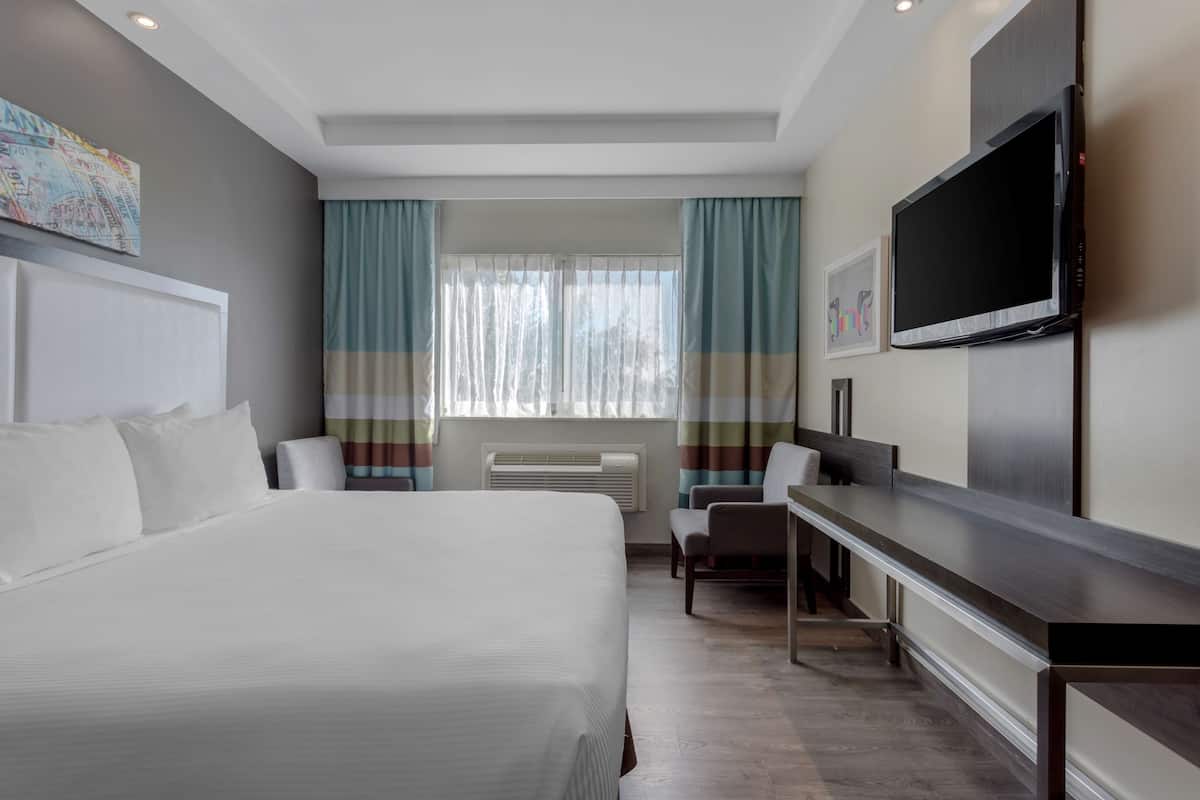 A hotel room with a large bed, a desk, a chair, a flat-screen TV, and a window with curtains.