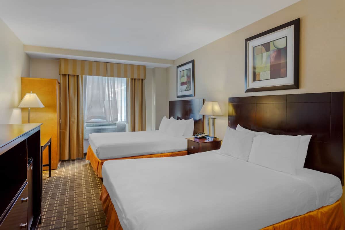 A hotel room with two beds, a desk, a chair, and a window with curtains.