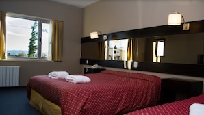 Una habitación de hotel con una cama grande, una mesita de noche con lámpara, un espejo y una ventana con cortinas.