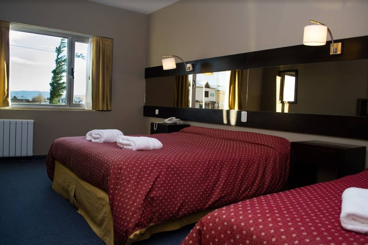 Een hotelkamer met een groot bed, een nachtkastje met een lamp, een spiegel en een raam met gordijnen.