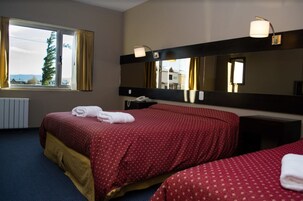 Una habitación de hotel con una cama grande, una mesita de noche con lámpara, un espejo y una ventana con cortinas.