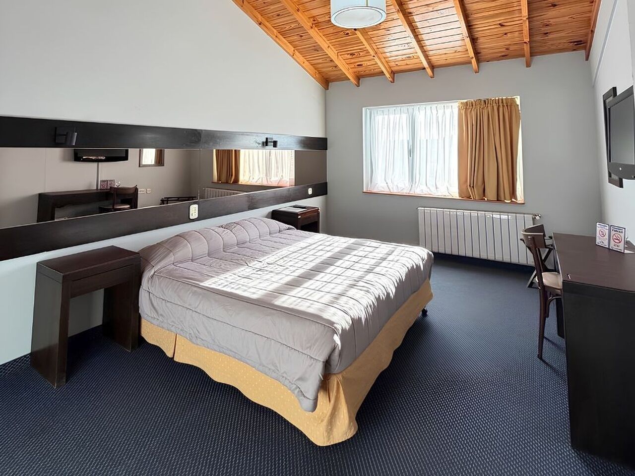 A bedroom with a bed, a desk, a chair, a mirror, a window with curtains, and a ceiling fan.
