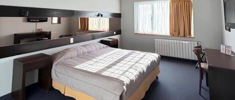 A bedroom with a bed, a desk, a chair, a mirror, a window with curtains, and a ceiling fan.