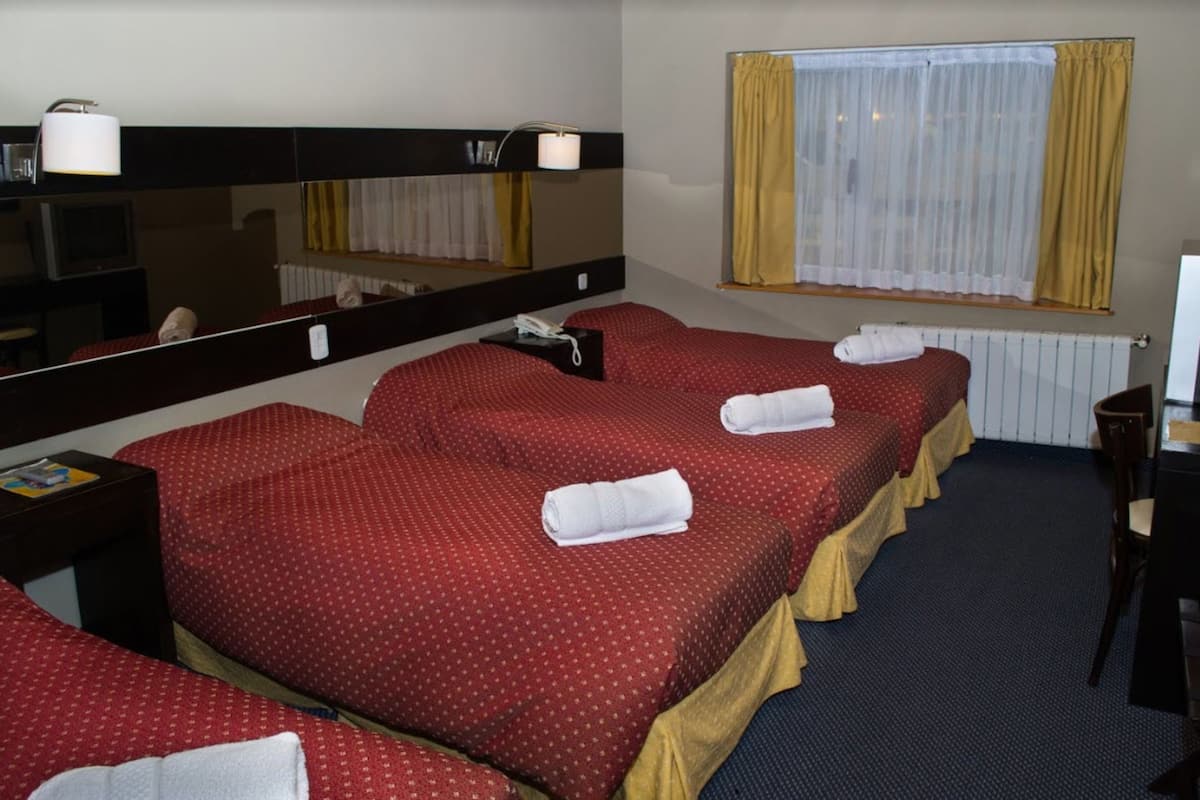 Een hotelkamer met drie enkele bedden, een grote spiegel, een bureau met stoel en een raam met gordijnen.