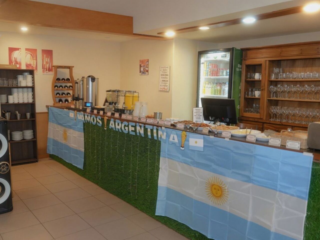 Een buffetgedeelte met een tafel, een vlag, een koffieapparaat en een koelkast.