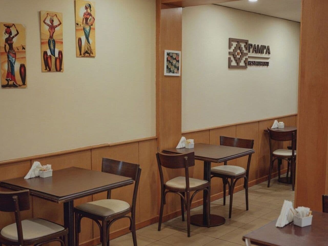A restaurant interior with wooden tables and chairs, a wall-mounted sign, and artwork.