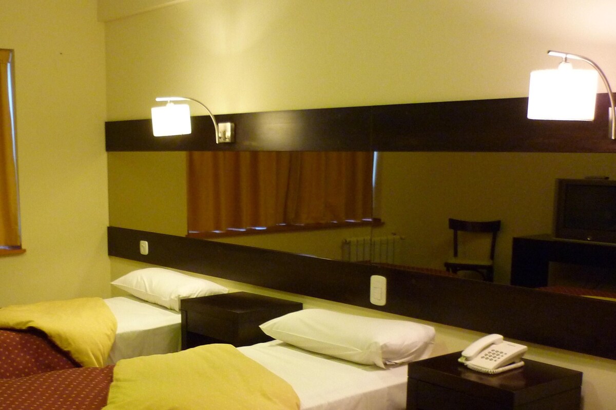 Une chambre d’hôtel avec deux lits, une table de chevet avec un téléphone, un miroir et des rideaux.
