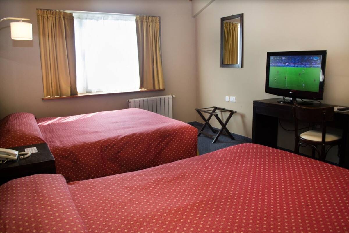 Een hotelkamer met twee bedden, een bureau met stoel, een televisie en een raam met gordijnen.
