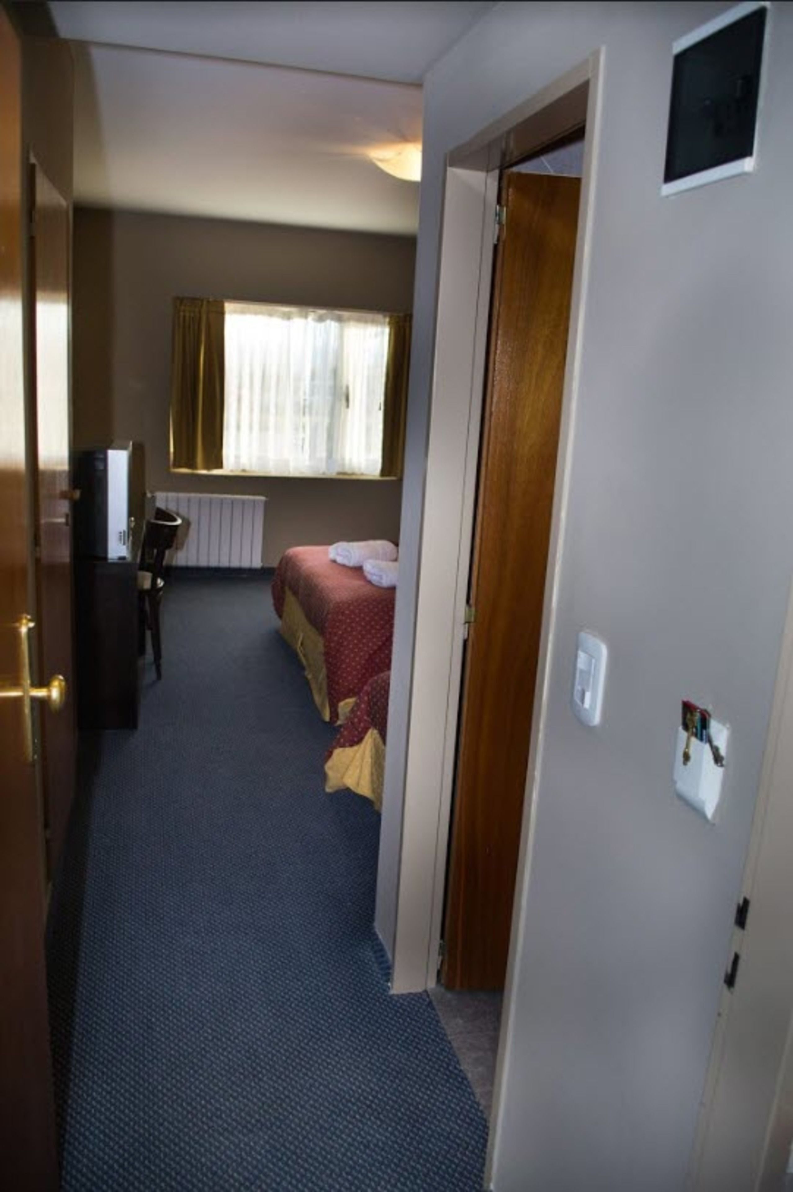 A narrow hallway leading to a bedroom with a bed, a desk, and a chair.