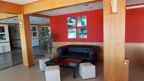 Un hall con un sofá de cuero negro, otomanas blancas, una mesa de centro de vidrio y paredes rojas decoradas con carteles de viajes.