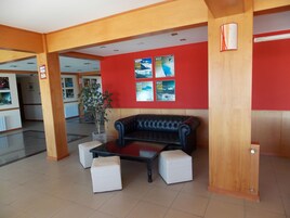 Un hall con un sofá de cuero negro, otomanas blancas, una mesa de centro de vidrio y paredes rojas decoradas con carteles de viajes.
