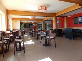 Un restaurante amplio con mesas y sillas de madera, una zona de recepción y una pantalla de televisión en la pared.