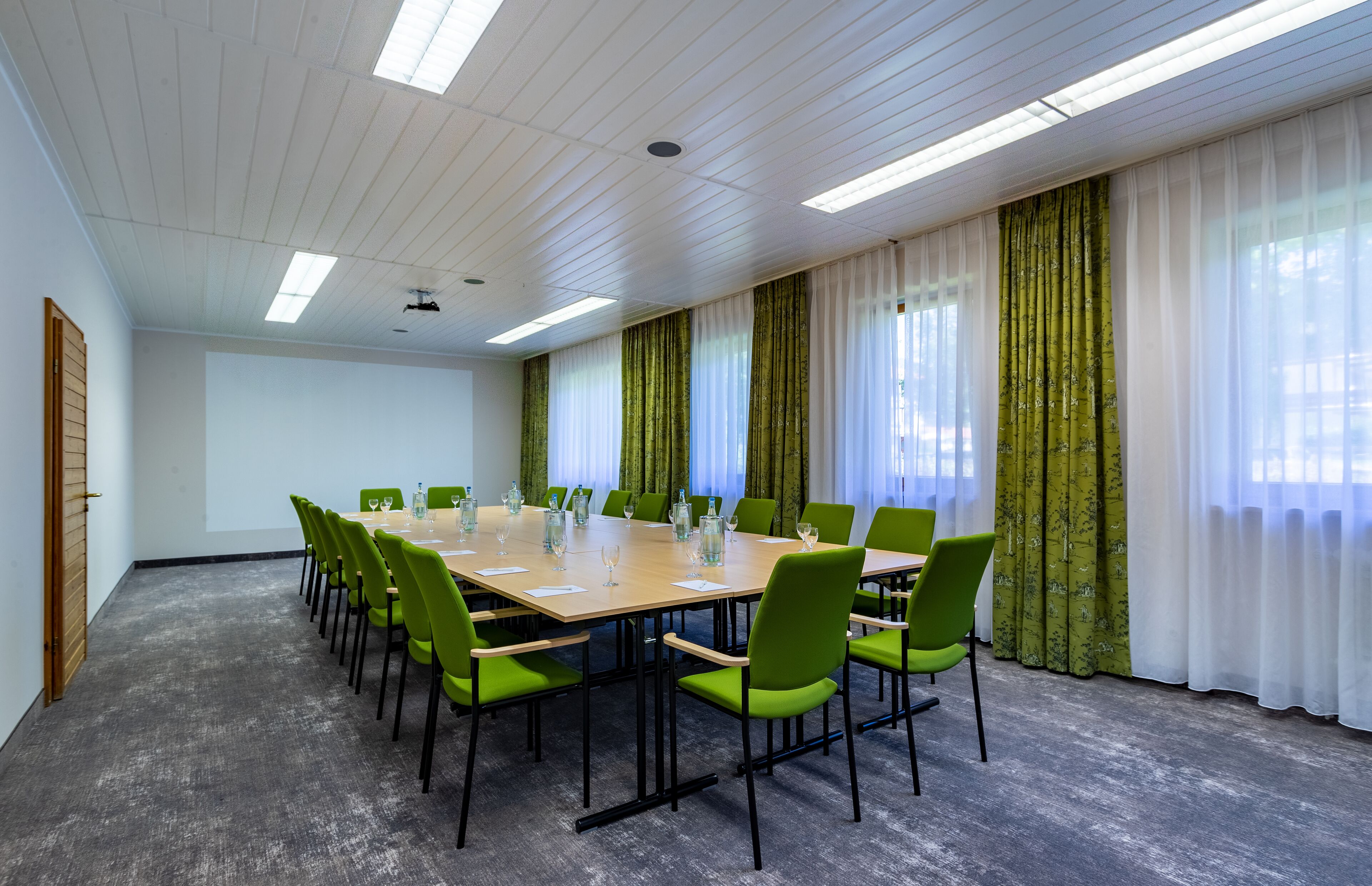 A conference room with a long table, green chairs, and white curtains.