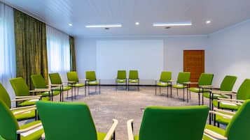 Un salón de conferencias con sillas verdes dispuestas en semicírculo, paredes blancas y una puerta de madera.