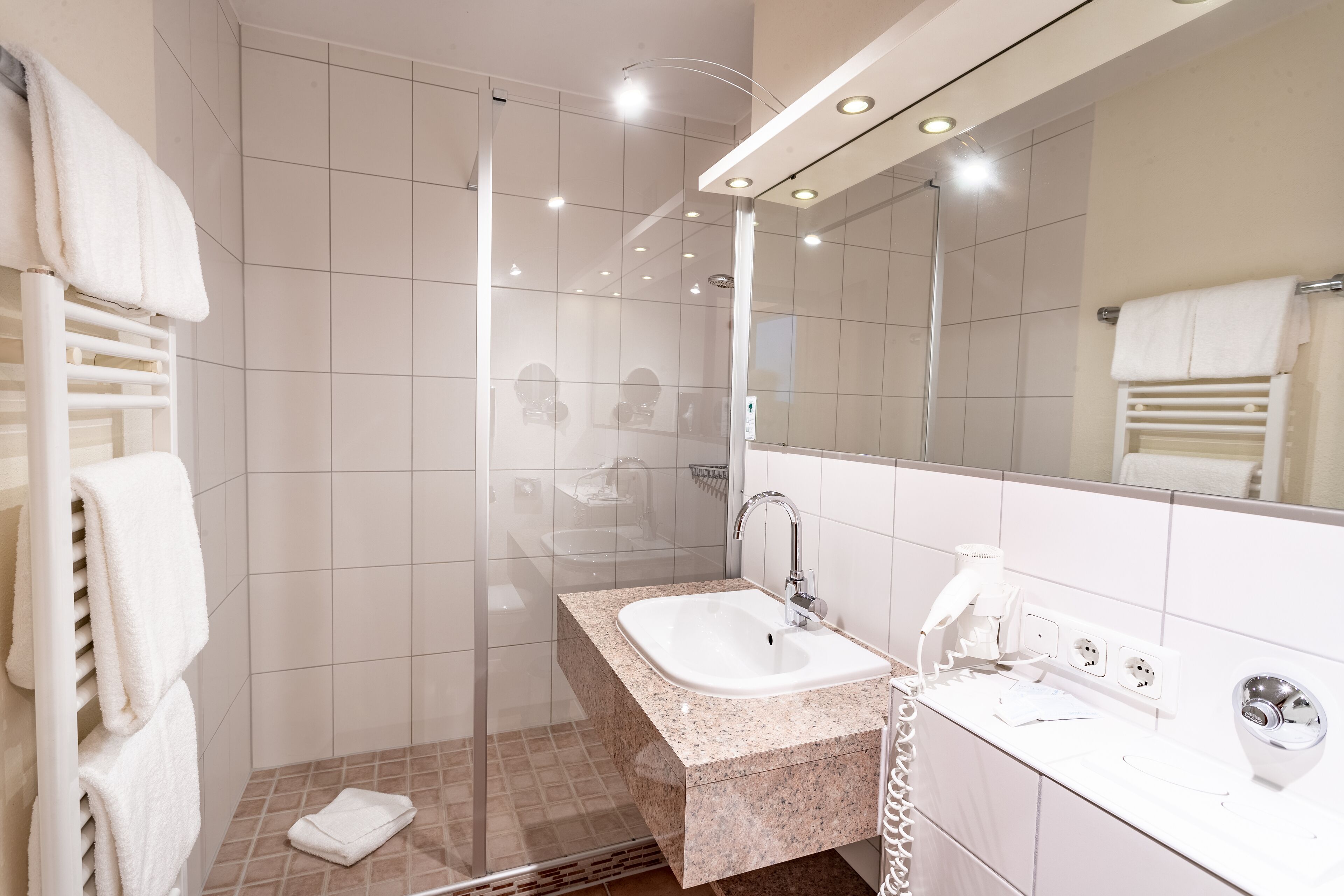A modern bathroom with a glass shower enclosure, a standalone sink, and a large mirror.